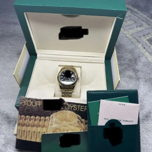 Guldfärgad klocka med svart urtavla - Elegant guldfärgad klocka med en stilren svart urtavla. Klockan har en klassisk länkarmband i guld och kommer i originalförpackning med tillhörande dokumentation. Perfekt för den som söker en tidlös accessoar. För mer INFO KOM PM