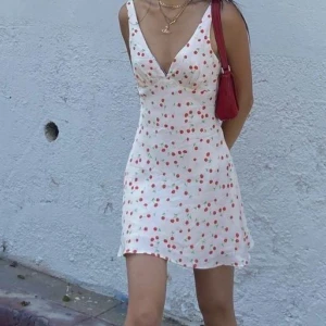  kortklänning med körsbärsmönster - Söt off white kortklänning med körsbärsmönster och v-ringad design. Perfekt för sommardagar med sin lätta och luftiga stil. Klänningen har smala axelband och en figurnära passform som ger en feminin look.(pris kan diskuteras 🥰)