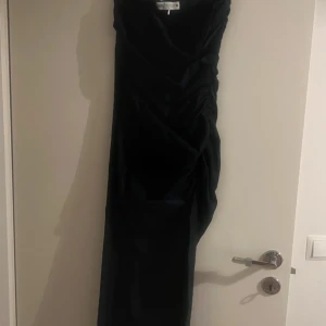 Marinblå långklänning - Elegant marinblå långklänning med draperad design. Perfekt för en stilfull kväll. Klänningen har en smickrande passform och är tillverkad i ett mjukt material som ger en lyxig känsla, slits finns. Oanvänd. 