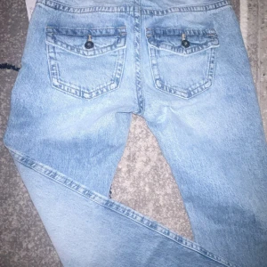 Ljusblå y2k jeans - Snygga ljusblå jeans med klassisk femficksdesign och knappdetaljer på bakfickorna. De har en rak passform och är perfekta för en avslappnad stil. Jeansen har en midwaist och är tillverkade i denim. Sitter som bootcut jeans!