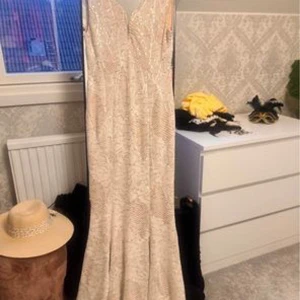 Elegant långklänning - Säljer en superfin vit/beige långklänning i spets. Den har en v-ringad design och är perfekt för festliga tillfällen. Klänningen är ärmlös och har en elegant passform som framhäver figuren. Perfekt för sommarens alla fester!