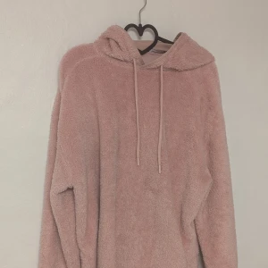 Rosa fluffig hoodie från Busem, strl L - Supermysig rosa hoodie från Busem i storlek L. Perfekt för kalla dagar med sitt fluffiga material och stora huva. Den har långa ärmar och en avslappnad passform.