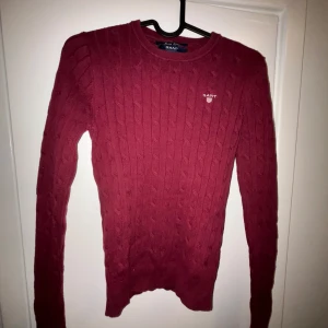 Röd stickad tröja från GANT - Säljer en snygg röd stickad tröja från GANT i storlek XS. Tröjan har ett klassiskt kabelstickat mönster och är perfekt för både höst och vinter. Den är långärmad och supermysig att ha på sig. Passar perfekt till både jeans och kjol!