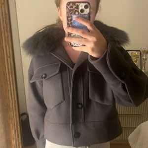 Grå Meotine jacka med pälskrage - Säljer en snygg grå jacka med pälskrage och stora knappar från Meotine! Den har en croppad stil och är perfekt för höst och vinter. Jackan har långa ärmar och stora fickor framtill. Den är i mycket gott skick! Storlek M/S! Jag kan mötas upp i Stockholm men kan också frakta!