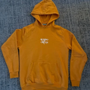 Orange hoodie med tryck - Säljer en snygg orange hoodie från Running in Circles i storlek S. Den har ett coolt tryck på framsidan och en klassisk känguruficka. Perfekt för höst och vår när du vill vara både bekväm och stilren. Huvan är mjuk och skön, perfekt för kyliga dagar. 🧡