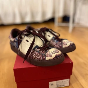 Valentino Garavani sneakers i blommigt mönster - Säljer ett par unika Valentino Garavani sneakers i storlek 38. Skorna har ett färgglatt blommigt mönster med inslag av vinrött och beige. De är i mycket bra skick och kommer i originalförpackning. Perfekta för att ge din outfit en lyxig touch! Säljer pga att dom har blivit för små❤️