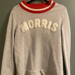 Grå sweatshirt från Morris - Säljer en snygg grå sweatshirt från Morris med texten 'MORRIS' i vit frotté på bröstet. Den har en cool ribbad krage i rött och vitt som ger en sportig look. Perfekt för både vardag och chill! 🩶