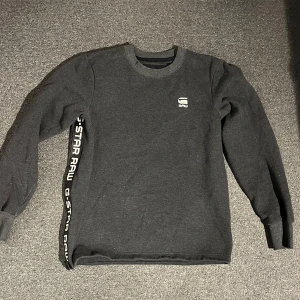 Svart tröja från G-Star RAW - Säljer en svart långärmad tröja från G-Star RAW i mycket bra skick. Den har en stilren design med logotypen tryckt på bröstet och längs sidan. Perfekt för både vardag och avslappnade tillfällen. Passar bra till jeans eller joggers!