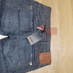 Mörkblå jeans från Cycle - Säljer ett par snygga mörkblå jeans från Cycle i nytt skick. De har en klassisk femficksdesign och en cool läderdetalj vid midjan. Perfekta för både vardag och fest! 🕺