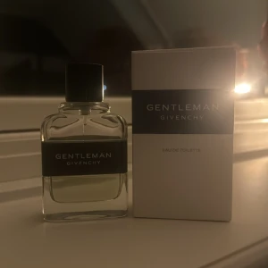 Gentleman Givenchy Eau de Toilette - Säljer en elegant och stilren flaska av Gentleman Givenchy Eau de Toilette. Flaskan är genomskinlig med en svart etikett och svart kork. Doften är klassisk och maskulin, perfekt för speciella tillfällen eller vardagsbruk. Kommer i originalförpackning.