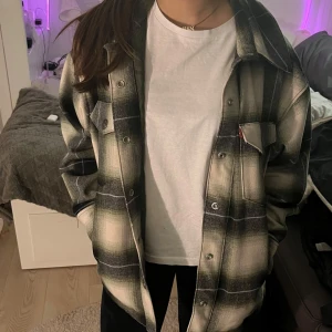 Rutig overshirt från Levi's - Säljer en snygg rutig overshirt från Levi's i storlek XS. Den har en cool svart och beige färgkombination med knappar framtill och två bröstfickor. Perfekt för höst och vår när du vill ha en avslappnad men stilren look. Knappt andvänd har använt den ca 3-5 gånger. Original pris är ca 2000kr  köpte den för ca 2 år sen, priset går att diskuteras