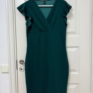 Grön klänning från Shein - Snygg grön klänning från Shein i storlek L. Den har en v-ringad design med volangdetaljer på ärmarna. Perfekt för både fest och vardag. Klänningen är i ett mjukt och bekvämt material som ger en smickrande passform. Helt ny och oanvänd, perfekt för julen och nyåret som närmar sig! 