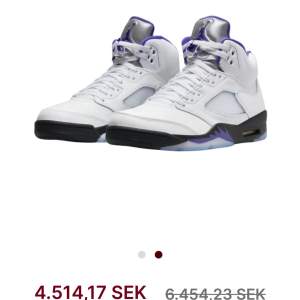 Säljer ett par Nike Air Jordan 5 Retro i vitt med snygga lila detaljer. Skorna har en cool design med snörning och en bekväm passform. Perfekta för både vardag och fest! De är i nytt skick och kommer i originalkartong. Har även sparat Jordans Lace Lock som kommer med i Boxen.