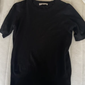 Svart kortärmad topp - Säljer en stilren svart topp i mycket bra skick. Den har en klassisk design med korta ärmar och rund hals. Perfekt för både vardag och festliga tillfällen. Passar bra till jeans eller kjol för en avslappnad look.