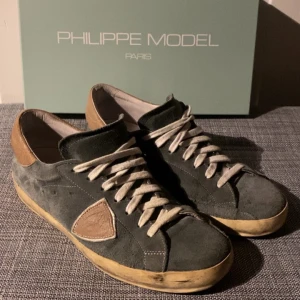 Philippe Model sneakers i mocka - Säljer ett par snygga Philippe Model sneakers i grå mocka med bruna detaljer. Perfekta för både vardag och festliga tillfällen! Riktigt sköna och väldigt bra skick, inga skador nånstans! Box medföljer!