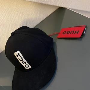 Hugo boss keps - Snygg svart keps från Hugo i nytt skick. Den har en vit broderad logga framtill och en klassisk design. Perfekt för både vardag och fest. Kepsen är i en stilren och tidlös stil som passar till det mesta.