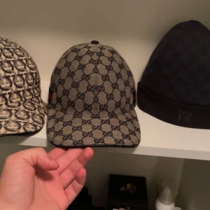 Grå/blå gucci keps  - Säljer en snygg grå/blå keps från Gucci med det klassiska GG-mönstret. Kepsen har en justerbar rem baktill och en röd och blå rand på sidan. Perfekt för att ge din outfit en lyxig touch! OBS! Kepsen är helt ny använt max 7 gånger, inga defekter eller sådant på kepsen. Har ett kvitto men tyvär ingen dustbag mm.