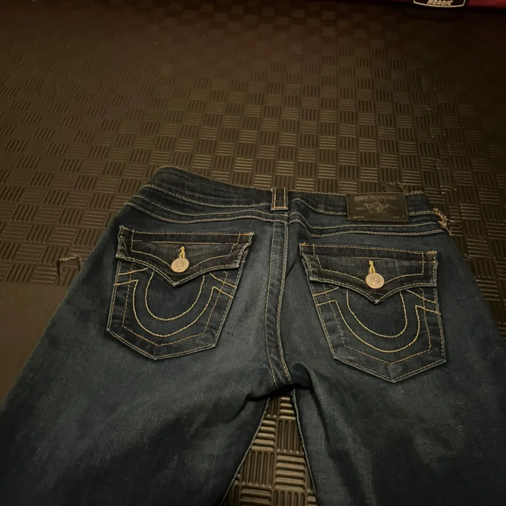 Säljer ett par as snygga mörkblå jeans från True Religion i storlek 25. De är bootcut och har låg midja med coola detaljer på bakfickorna. Funkar till bokstavligen allt!. Jeans & Byxor.