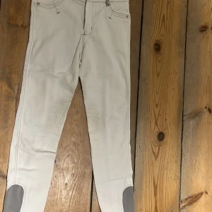 Vita ridbyxor med dragkedja - Säljer ett par vita ridbyxor i bra skick. De har en dragkedja fram och förstärkningar vid knäna. Perfekta för ridning och har en tight passform. Några små fläckar finns, men inget som stör funktionen. Passar perfekt för både träning och tävling. Jag vet inte storlek men då lappen är bortklippt men dom är 93-94 cm långa och 35 cm breda i märket covalliero 