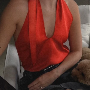 Röd halterneck topp - Snygg röd halterneck topp i ett glansigt material. Perfekt för festliga tillfällen med sin djupa urringning och knytning i nacken. Toppen har en smickrande passform och är både stilren och trendig. Aldrig använt💓