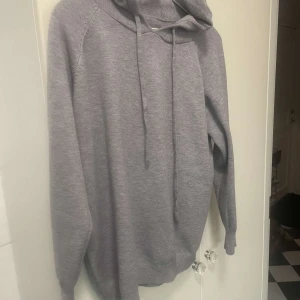 Grå stickad hoodie - Säljer en stilren grå hoodie i mjukt bomullsmaterial. Perfekt för både höst och vinter med sin mysiga känsla. Den har rätt så korta ärmar och en klassisk huva med dragsko. Passar till alla tillfällen när du vill vara bekväm och snygg. Strl xs-s. Den är från Verani clothing 