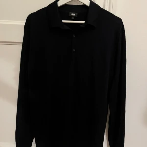 Mörkblå långärmad pikétröja från Uniqlo - Säljer en stilren svart långärmad pikétröja från Uniqlo. Perfekt för både vardag och lite mer uppklädda tillfällen. Tröjan har en klassisk krage och knappar framtill. Passar bra till jeans eller chinos för en avslappnad look.