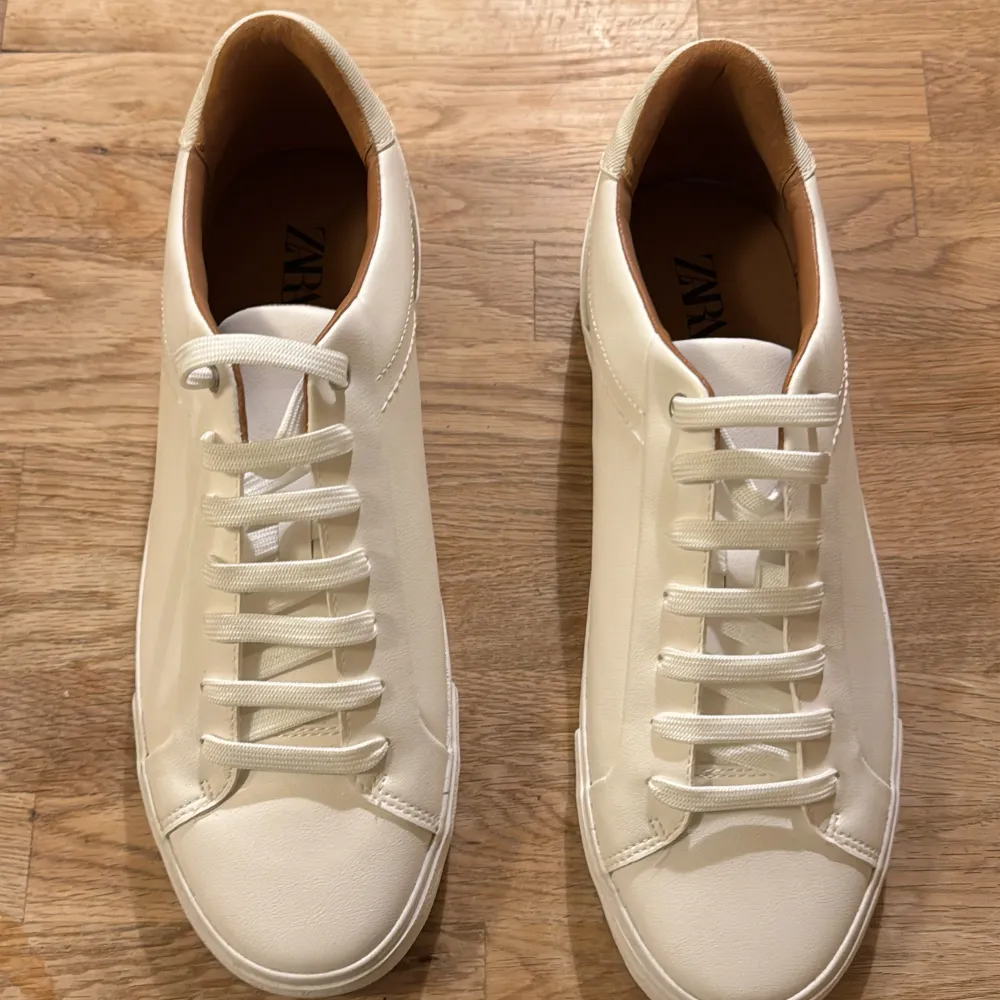 Säljer ett par stilrena vita sneakers från Zara i nytt skick. De har en klassisk design med snörning och är perfekta för både vardag och fest. Skorna är gjorda i syntetmaterial och har en bekväm passform. Perfekta för vår och sommar! . Skor.