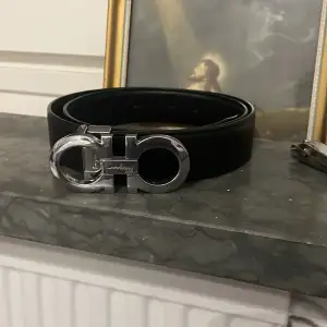 Säljer ett elegant svart skärp från Salvatore Ferragamo med en stilren silverfärgad spänne. Perfekt för att ge en lyxig touch till vilken outfit som helst. Skärpet är i mycket bra skick och passar både till vardag och fest. Pris ej hugget i sten 