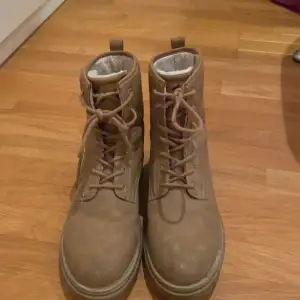 Säljer ett par bruna boots från Rest i bra skick. De är i storlek 41 och har en robust design med snörning framtill. Perfekta för höst och vinter med sitt varma foder. Skorna är tillverkade i ett slitstarkt material som passar för kyligare väder.