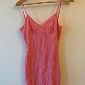 Rosa ribbad kort klänning - Säljer en superfin rosa ribbad klänning med smala axelband. Perfekt för sommardagar eller en avslappnad fest. Klänningen har en enkel och stilren design som gör den lätt att matcha med olika accessoarer.
