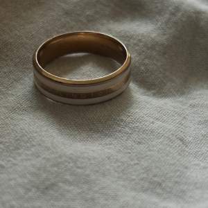 Säljer en stilren ring i guld och vit. Den har en slät yta med en subtil design som passar perfekt för både vardag och fest. Ringen är i mycket bra skick och har en inskription på insidan. Perfekt för dig som gillar minimalistisk stil! Pris kan diskuteras 