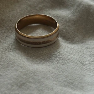 Elegant Ring Daniel Wellington  - Säljer en stilren ring i guld och vit. Den har en slät yta med en subtil design som passar perfekt för både vardag och fest. Ringen är i mycket bra skick och har en inskription på insidan. Perfekt för dig som gillar minimalistisk stil! Pris kan diskuteras 