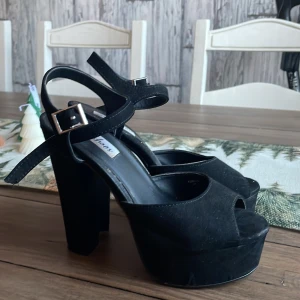 Svarta platåpumps med remmar - Snygga svarta platåpumps med hög klack och justerbara remmar. Perfekta för en utekväll eller fest. De har en öppen tå och är i mycket bra skick. Stilrena och lätta att matcha med olika outfits.