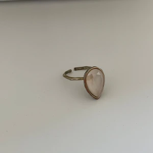Ring LILLY AND ROSÉ  - Snygg ring med en stor droppformad sten i en ljus nyans. Ringen har en justerbar metallbas i en antik guldton. Perfekt för att ge en elegant touch till vilken outfit som helst!