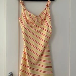 Randig klänning från ADOORE - Säljer en superfin randig klänning från ADOORE i storlek 40. Den har en härlig gul bas med röda ränder och smala axelband. Perfekt för sommardagar eller en avslappnad fest. Klänningen är aldrig använd och fantastiskt skick med en skön passform.