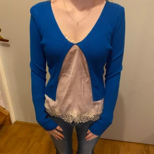 Blå ribbad bolero - Säljer en fin blå ribbad bolero med lång ärm. Perfekt för både vardag och fest! Den har en djup v-ringning och är i ett mjukt material som sitter skönt på kroppen. Passar bra över en topp/linne eller klänning. Storleken är normal och den är i mycket bra skick.