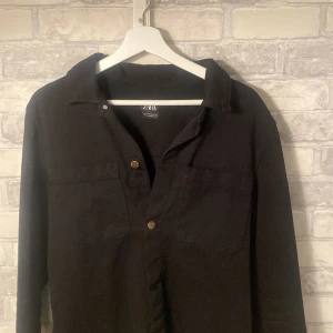 Svart Overshirts  från Zara - Säljer en stilren svart skjorta från Zara i storlek M. Skjortan har långa ärmar och knappar framtill. Perfekt för både vardag och festliga tillfällen. Den är i mycket bra skick och redo för en ny ägare!