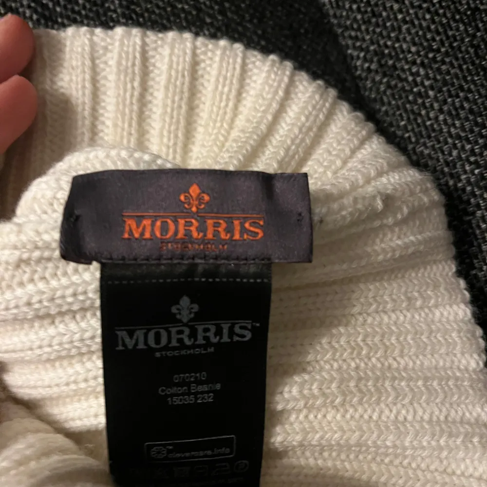 Säljer en snygg vit stickad mössa från Morris. Den är ribbad och har en uppvikt kant med en stilren logga framtill. Perfekt för att hålla sig varm under kyliga dagar. Passar både till vardags och mer uppklädda tillfällen.. Accessoarer.