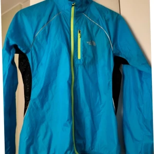 Turkos vind/ löpar jacka från The North Face - Säljer en turkos vindjacka från The North Face i bra skick. Jackan har en dragkedja i neonfärg och en liten bröstficka med dragkedja. Perfekt för vår och höst, och den är långärmad. Passar bra för utomhusaktiviteter.