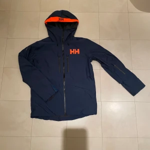 Helly Hansen Insulated Skidjacka - ENDAST ANVÄND EN SKIDDAG, köpte jackan då mitt bagage va försenat.  Färg: 453 Dark Creek Nypris: 5 000 kr (se på deras hemsida nedan) https://www.hellyhansen.com/sv_se/garibaldi-20-jacket-65747?color=631578   FUNKTIONER UTSIDA: 🟥: Justerbara ärmöppningar, midja & huva.  🟩: 2 framfickor med borstat foder, 2bröstfickor,  ficka för liftkort. 🟦: RECCO® Advanced Rescue-systemstransponder  INSIDA: 🟥: H2Flow™-ventilationssystem  🟩: LIFE POCKET+™ bevarar telefon batteri & nät innerficka 🟦: Snöskydd