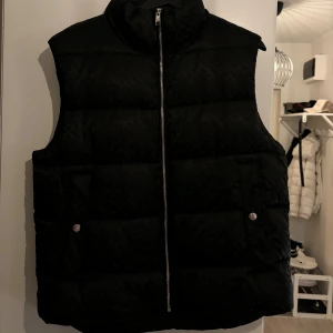 Svart dunväst från Hugo Boss - Säljer en snygg svart dunväst från Hugo Boss i mycket bra skick. Västen har en dragkedja framtill och två fickor med knappar. Perfekt för höst och vinter, och passar både till fest och vardag. Storleken är herr M 