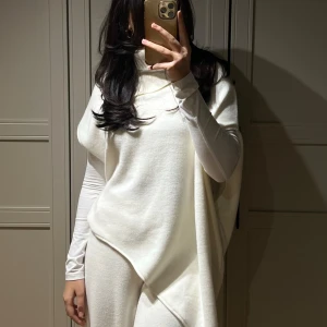 Vit asymmetrisk poncho - Säljer denna asymmetriska ‘t-shirt’-poncho med hög krage, köpt på Zara förra året. Den är gjord av ett mjukt och finstickat material. Eftersom tvättlappen saknas rekommenderar jag tvätt i låg temperatur och att undvika torktumlare. Den har endast använts 2-3 gånger och är i mycket bra skick.