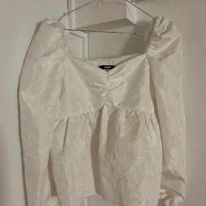Vit blus från Bik Bok - Säljer en superfin vit blus från Bik Bok. Den har långa ärmar och ett vackert blommigt mönster. Blusen är i ett luftigt material och har en smockad rygg för extra komfort. Storlek M. Använd fåtal gånger.