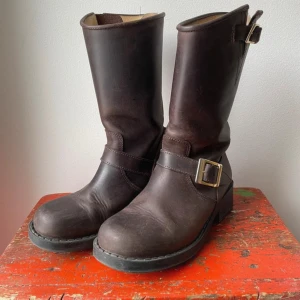 johnny bulls boots med spänne - Säljer ett par bruna boots i skinn med snyggt spänne på sidan. Perfekta för höst och vinter, dessa boots har en klassisk design som funkar till det mesta. De är i bra skick och redo för nya äventyr. Passar både till vardags och lite tuffare stilar.