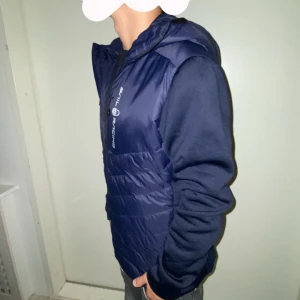 Mörkblå jacka från Sail Racing - Säljer en mörkblå jacka från Sail Racing i nytt skick. Jackan har en quiltad design med dragkedja och huva. Perfekt för höst och vår, med långärmade ärmar och en stilren look. Passar både till vardags och lite mer avslappnade tillfällen.
