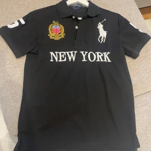 Svart pikétröja från Ralph Lauren - Säljer en snygg svart pikétröja från Ralph Lauren. Tröjan har en klassisk krage och knappar framtill. 