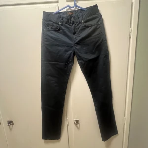Svarta byxor från J.Lindeberg - Snygga svarta byxor från J.Lindeberg med en klassisk design. Byxorna har en normal passform och är tillverkade i ett slitstarkt material. Perfekta för alla tider