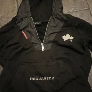 Svart hoodie från Dsquared2 - Snygg svart hoodie från Dsquared2 med dragkedja och logotypdetaljer. Perfekt för en casual look med stil. Den har en praktisk ficka framtill och en justerbar huva.