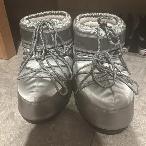 Silver Moon Boots med snörning - Snygga och varma silver Moon Boots med snörning. Perfekta för kalla vinterdagar. De har en glansig yta och är designade för att hålla fötterna varma och torra. De har ingen defekter, och jag fick de i julklapp för 2 år sen. De är i storlek 41 och passar mig som har 40 och de är lite stora.