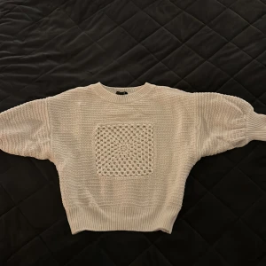 Vit stickad tröja från Lindex - Säljer en vit stickad tröja från Lindex med ett unikt stickat mönster på framsidan. Tröjan har puffiga ärmar och ribbstickade muddar vid ärmslut och nederkant. Perfekt för kyliga dagar!